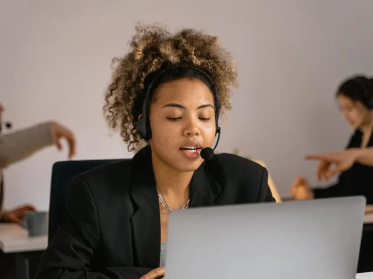 Mujer con auriculares de atención al cliente hablando frente a un laptop, representando un agente virtual atendiendo consultas